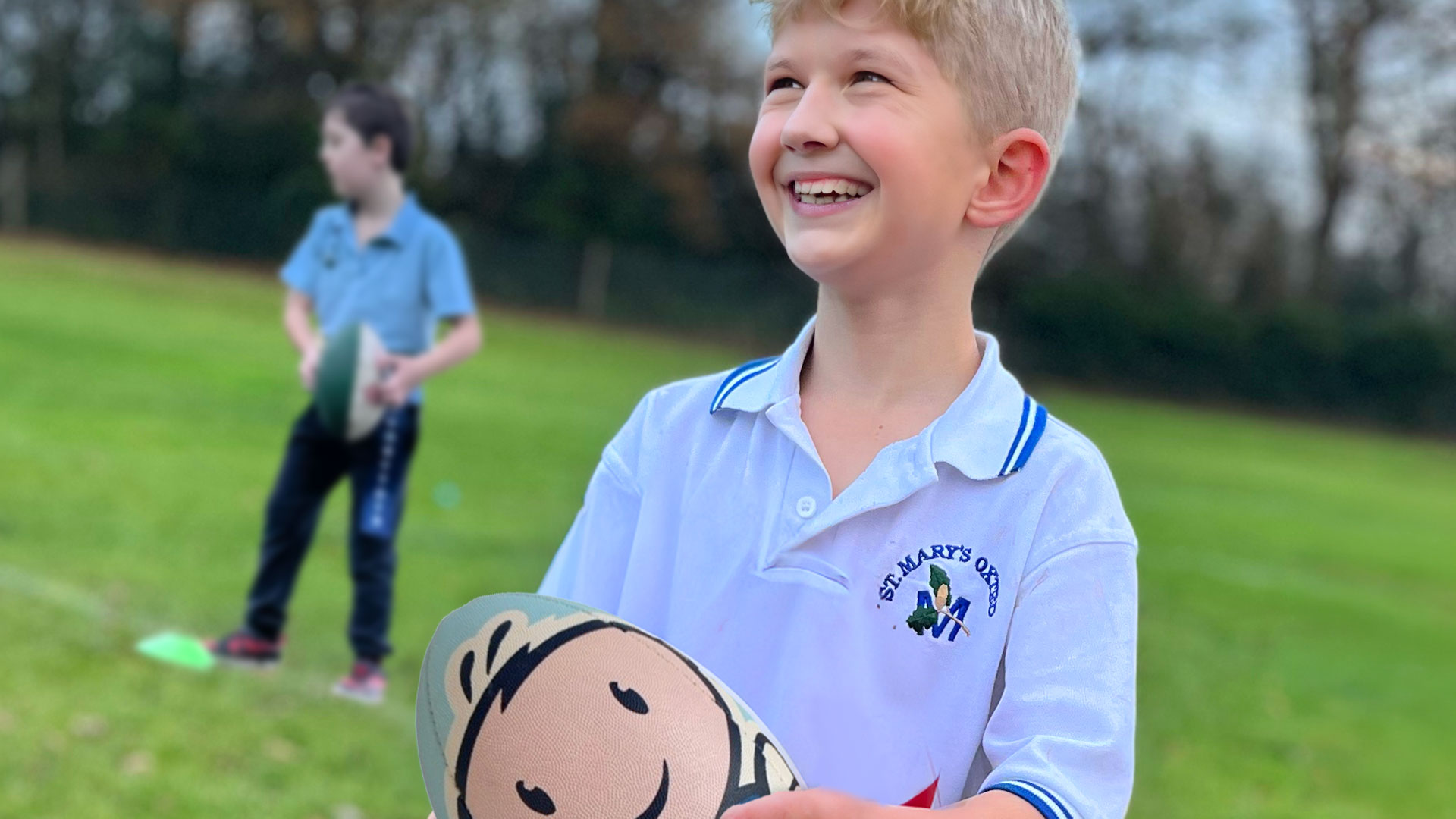 School boy on playing field holding a Rugbytots rugby ball.
