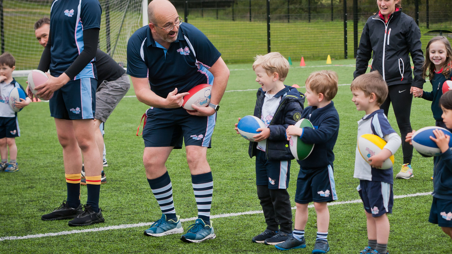 Children outdoors on a sports pitch with their Rugbytots coach.