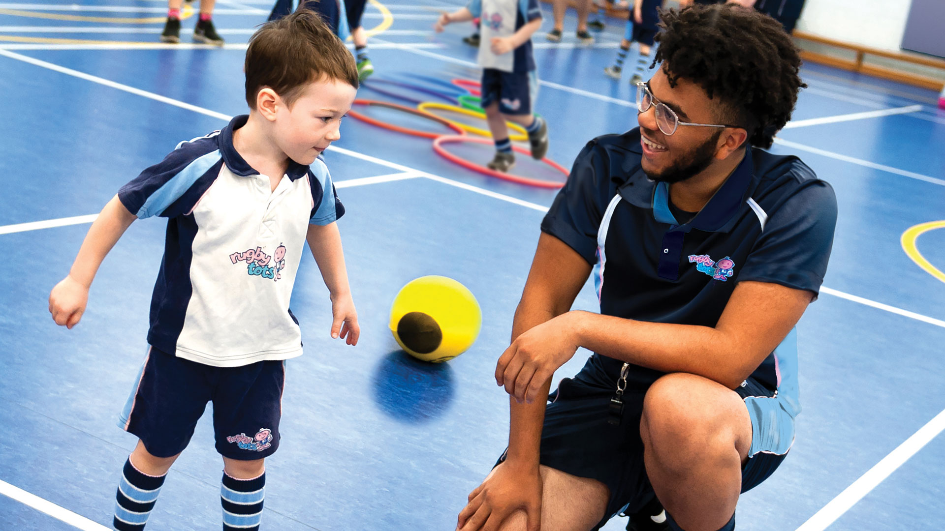 A friendly Rugbytots coach helping a boy with his rugby skills.