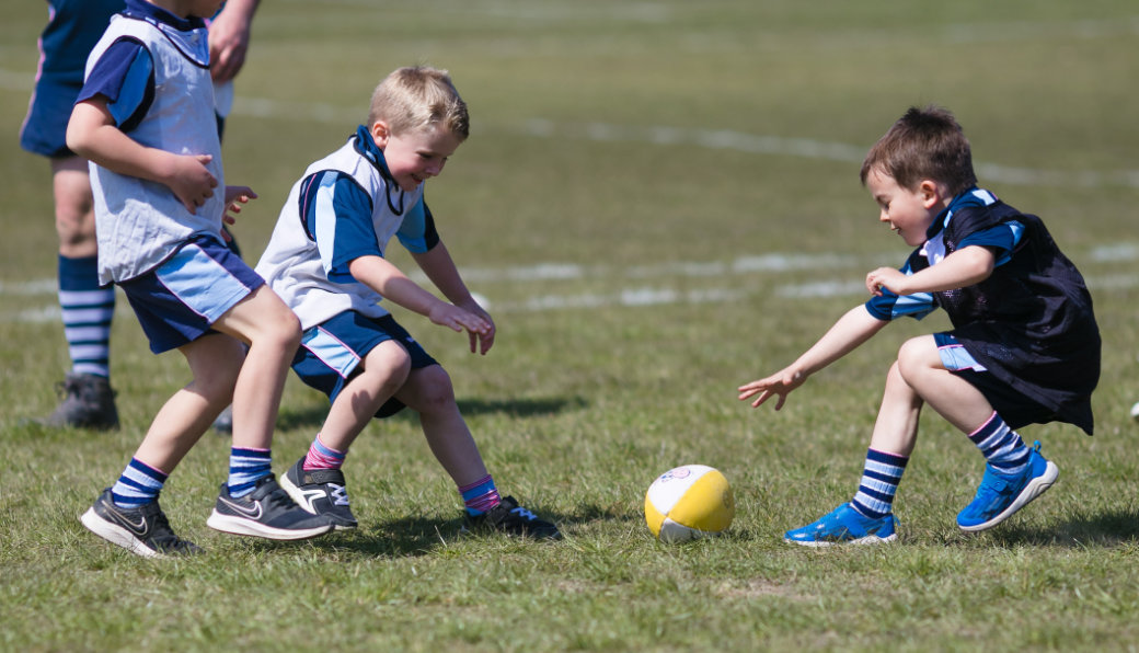 Group of smiling children holding party balloons and rugby balls for kids rugby party